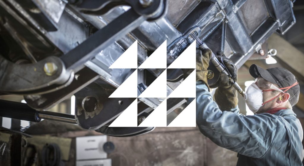 Mechanic wearing safety goggle and mask, working on heavy machinery with Kilkeel Harbour Works Logo overlayed.