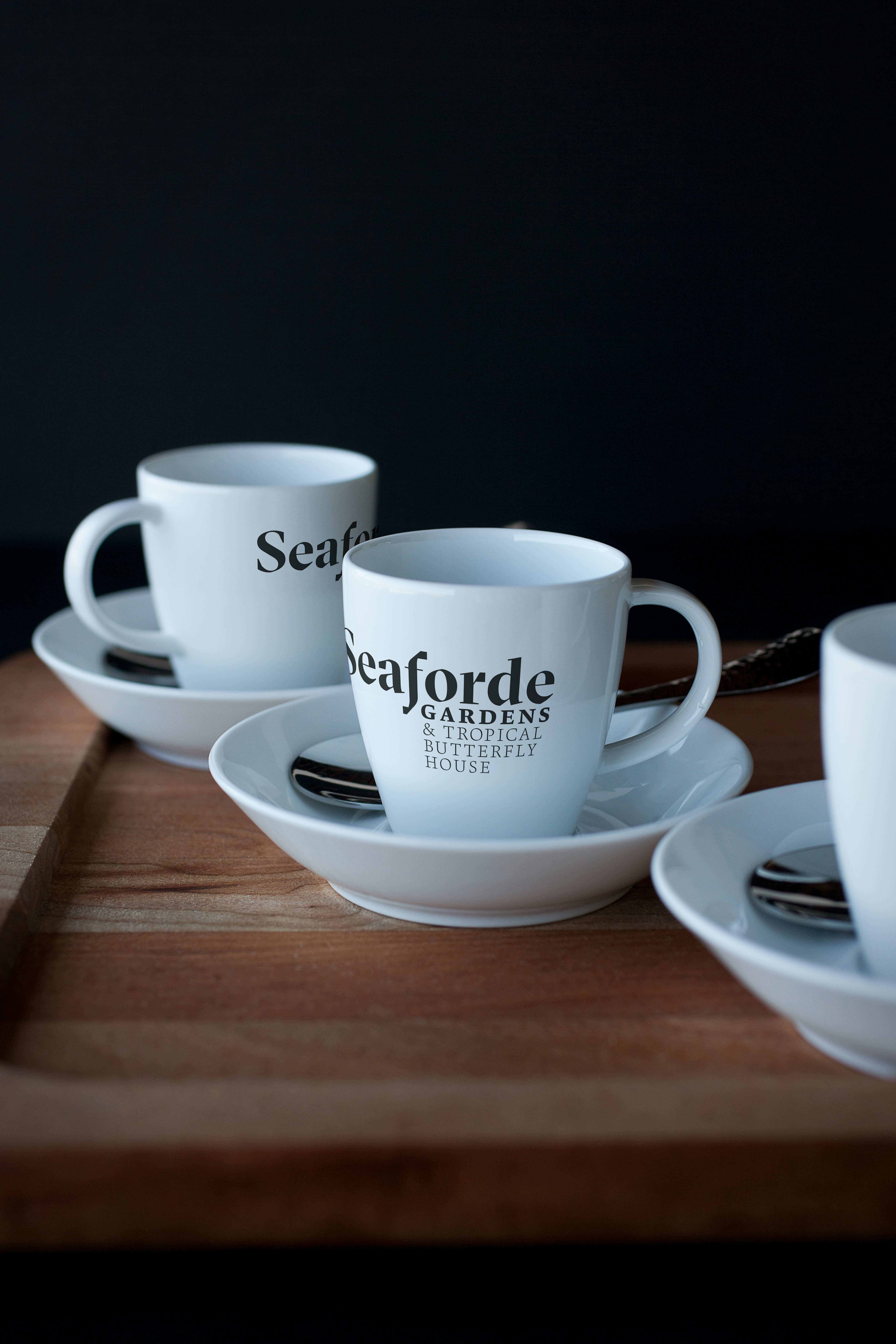 Three white espresso cups with green Seaforde Gardens logo printed on their sides.